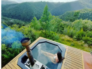 A woman in a Carbo III Wood Fired Hot tub overlooking forested mountains.